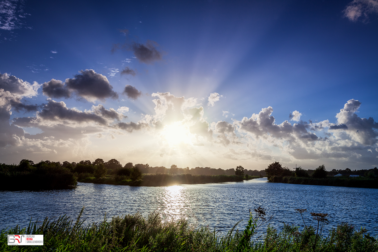 Zonnestralen vanachter de wolken vandaan over het water in Schipsloot Roderwolde Drenthe